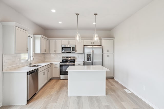 kitchen with hanging light fixtures, white cabinetry, stainless steel appliances, sink, and a center island