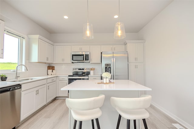 1703 Gordon Ct, Norwalk, IA 50211 - kitchen featuring appliances with stainless steel finishes, light wood-style floors, tasteful backsplash, a kitchen island, and white cabinetry