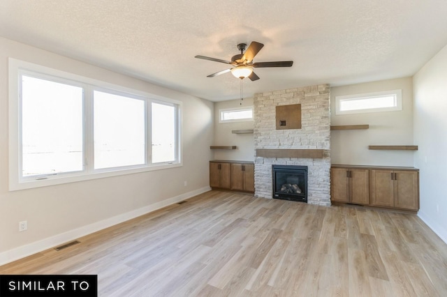 unfurnished living room with a stone fireplace, ceiling fan, light hardwood / wood-style flooring, and a textured ceiling