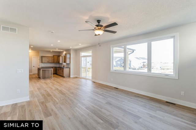 unfurnished living room featuring ceiling fan, sink, light hardwood / wood-style floors, and a textured ceiling