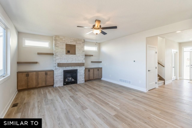 unfurnished living room with a stone fireplace, ceiling fan, and light wood-type flooring