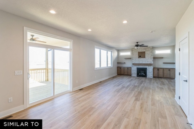 unfurnished living room with light hardwood / wood-style floors, a stone fireplace, and ceiling fan