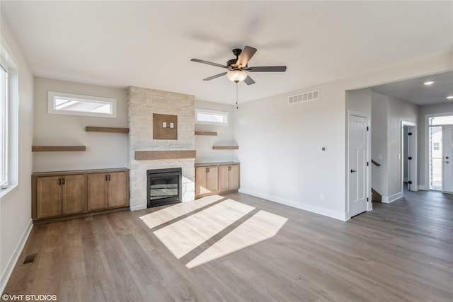 unfurnished living room with ceiling fan, a stone fireplace, and light hardwood / wood-style floors