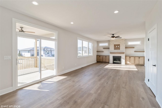 unfurnished living room featuring ceiling fan, a large fireplace, and light wood-type flooring