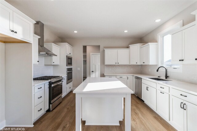 kitchen featuring sink, a center island, appliances with stainless steel finishes, wall chimney range hood, and white cabinets