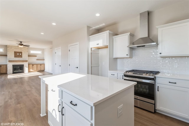 kitchen featuring wall chimney exhaust hood, white cabinetry, a center island, stainless steel range with gas stovetop, and hardwood / wood-style flooring