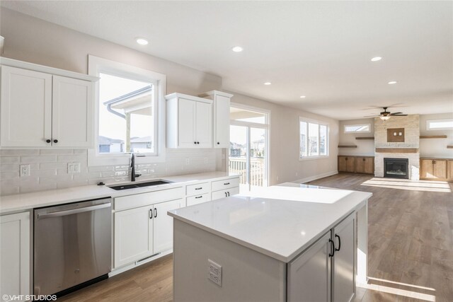 kitchen featuring sink, stainless steel dishwasher, a kitchen island, white cabinets, and backsplash