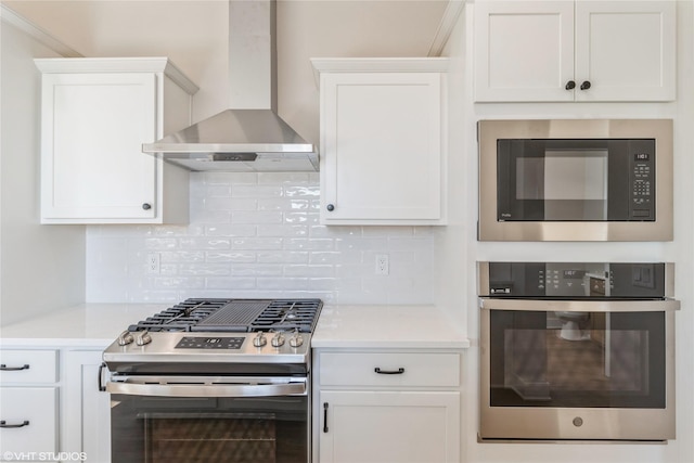 kitchen with wall chimney exhaust hood, white cabinetry, stainless steel appliances, and backsplash