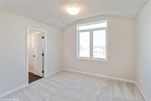 unfurnished room with vaulted ceiling, light colored carpet, and a textured ceiling