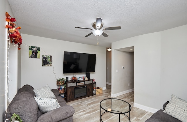 living room with a textured ceiling, light wood-type flooring, and ceiling fan