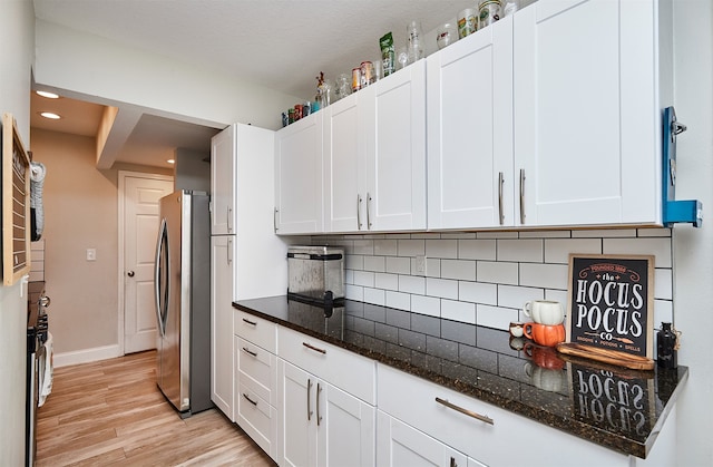 kitchen featuring stainless steel fridge, tasteful backsplash, light hardwood / wood-style flooring, white cabinetry, and dark stone counters