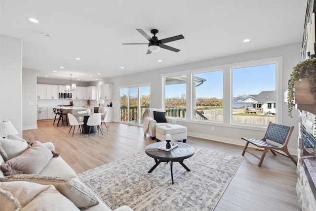 living room with ceiling fan with notable chandelier, light hardwood / wood-style flooring, and sink