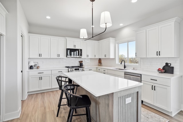 kitchen featuring sink, appliances with stainless steel finishes, decorative light fixtures, a kitchen island, and white cabinets