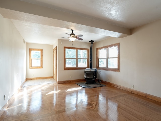 unfurnished living room with ceiling fan, light hardwood / wood-style flooring, a textured ceiling, and a wood stove