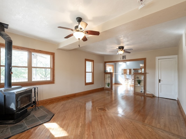 unfurnished living room with ceiling fan, hardwood / wood-style floors, a wood stove, and a healthy amount of sunlight