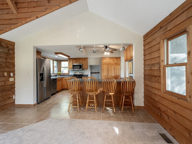 kitchen featuring ceiling fan, light tile patterned flooring, kitchen peninsula, appliances with stainless steel finishes, and vaulted ceiling