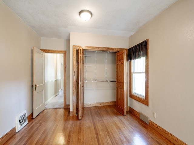 unfurnished bedroom with a textured ceiling, a closet, and light hardwood / wood-style flooring