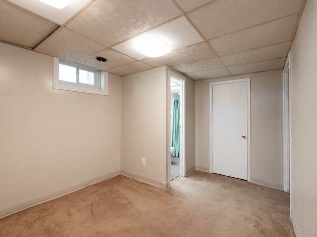 basement with a paneled ceiling and light colored carpet