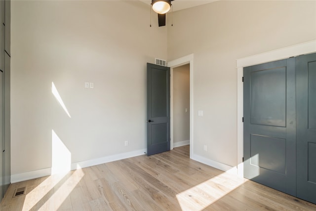 unfurnished bedroom with light wood-type flooring, ceiling fan, a closet, and a towering ceiling