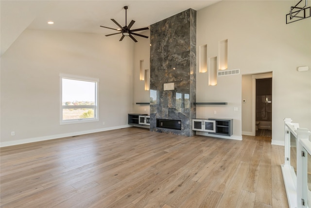 unfurnished living room with high vaulted ceiling, a tile fireplace, light hardwood / wood-style flooring, and ceiling fan