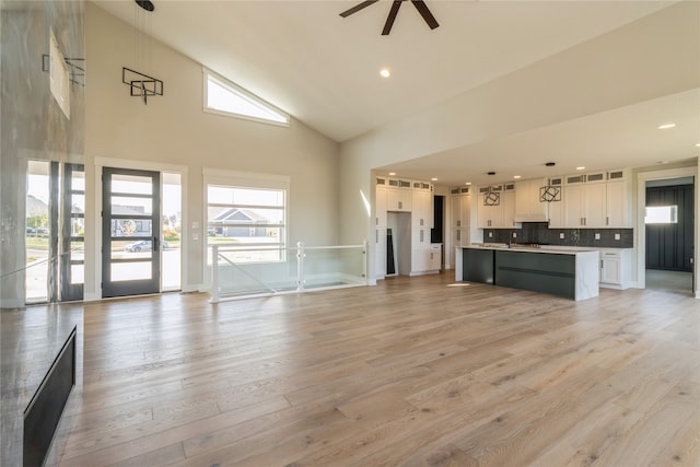 unfurnished living room featuring ceiling fan, light wood-type flooring, and high vaulted ceiling