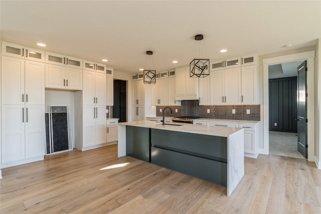 kitchen with hanging light fixtures, an island with sink, sink, and white cabinetry