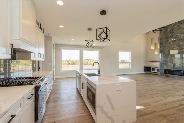 kitchen featuring white cabinets, an island with sink, sink, decorative light fixtures, and appliances with stainless steel finishes