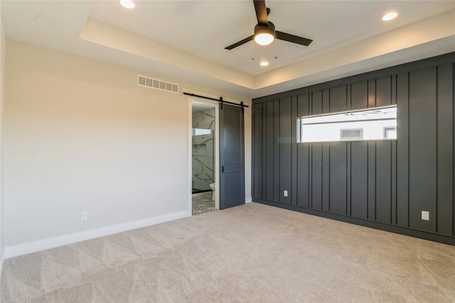 unfurnished bedroom with ceiling fan, light colored carpet, a tray ceiling, and a barn door