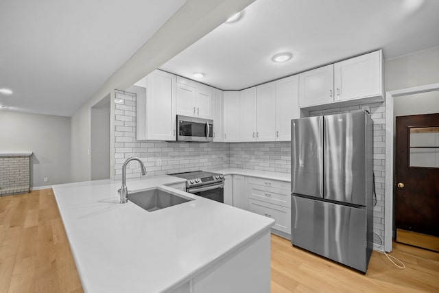 kitchen with kitchen peninsula, stainless steel appliances, sink, light hardwood / wood-style flooring, and white cabinets