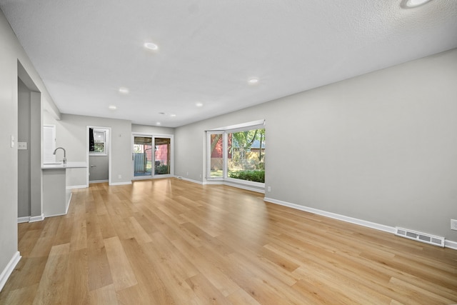 unfurnished living room featuring light hardwood / wood-style flooring and a textured ceiling