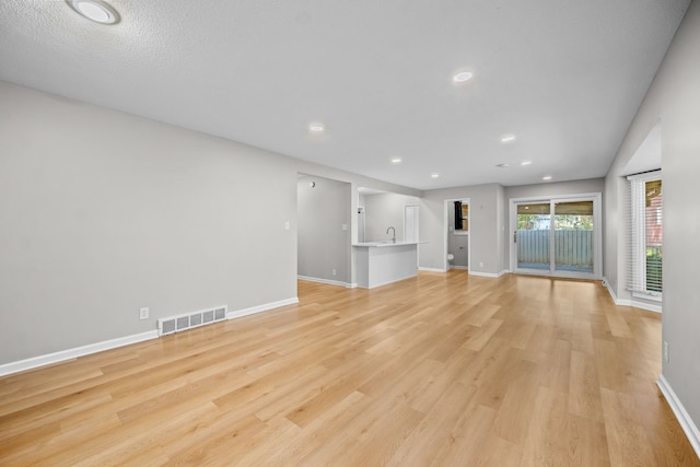 unfurnished living room with a textured ceiling and light hardwood / wood-style flooring