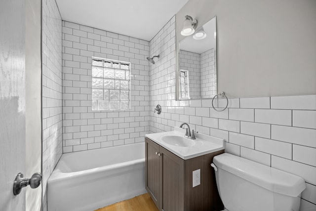 full bathroom featuring tiled shower / bath combo, wood-type flooring, toilet, vanity, and tile walls