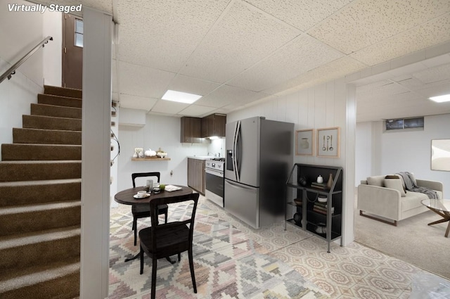 kitchen with a paneled ceiling, dark brown cabinets, light colored carpet, and appliances with stainless steel finishes