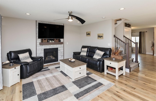 living room with a stone fireplace, light hardwood / wood-style flooring, and ceiling fan