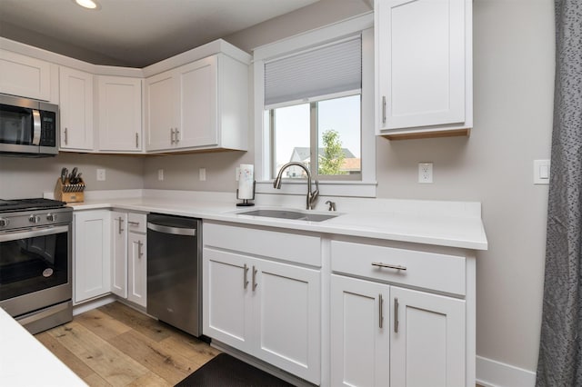 kitchen with a sink, white cabinetry, appliances with stainless steel finishes, light wood finished floors, and light countertops