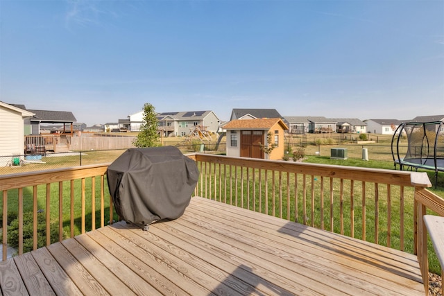 wooden deck featuring a storage shed, a trampoline, a lawn, and a residential view