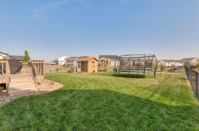 view of yard with a wooden deck, a fenced backyard, an outdoor structure, a trampoline, and a residential view