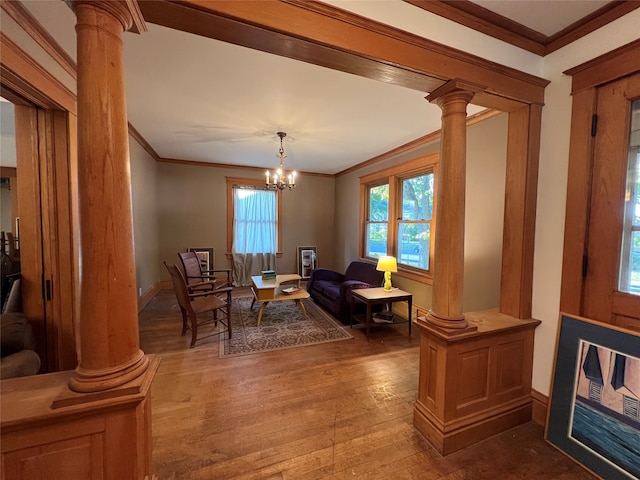 living area with decorative columns, crown molding, wood-type flooring, and a chandelier