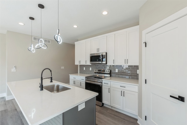 kitchen with sink, white cabinetry, appliances with stainless steel finishes, decorative light fixtures, and a center island with sink