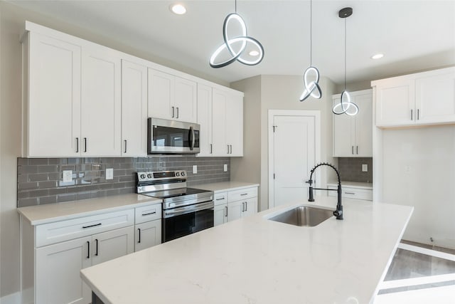 kitchen with a center island with sink, decorative light fixtures, sink, stainless steel appliances, and white cabinetry