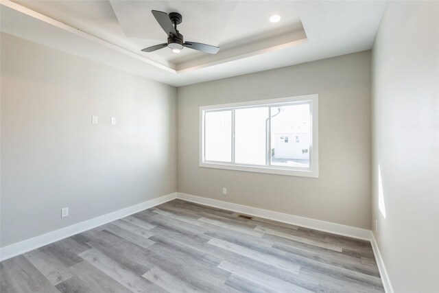 unfurnished room with ceiling fan, light hardwood / wood-style floors, and a raised ceiling