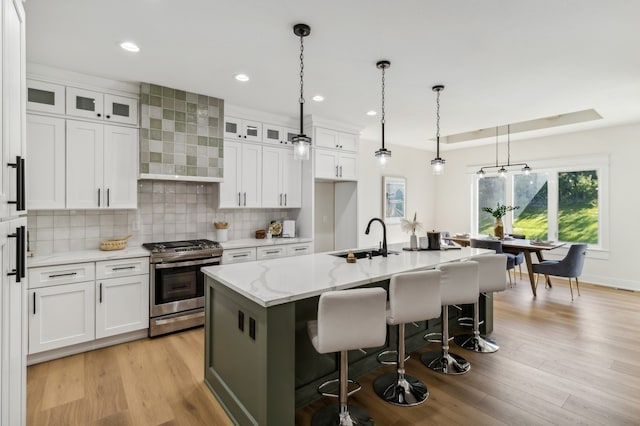 kitchen with stainless steel range with gas cooktop, sink, white cabinets, and a kitchen island with sink