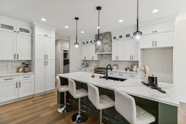 kitchen featuring a kitchen island with sink, sink, white cabinets, and wall chimney range hood