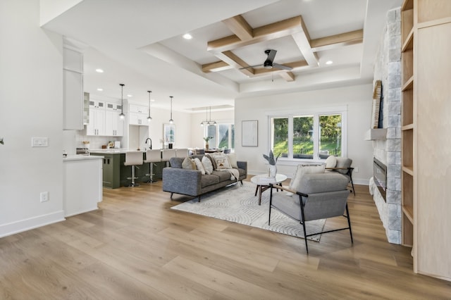 living room with coffered ceiling, sink, light hardwood / wood-style flooring, ceiling fan, and a fireplace