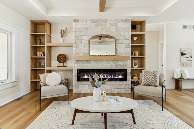 living area with built in features, light hardwood / wood-style flooring, and a stone fireplace