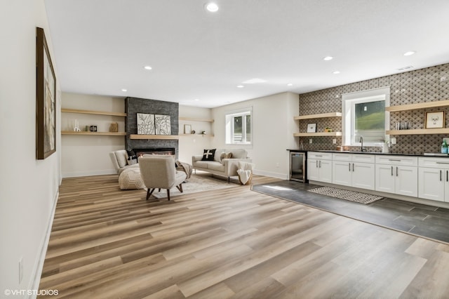 unfurnished living room with a fireplace, light wood-type flooring, wine cooler, and sink