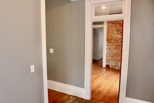 corridor with hardwood / wood-style flooring and brick wall