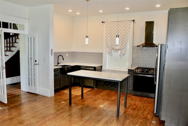 kitchen featuring hanging light fixtures, wall chimney range hood, appliances with stainless steel finishes, and hardwood / wood-style flooring