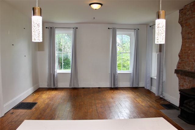 unfurnished living room with a wood stove, a healthy amount of sunlight, and dark hardwood / wood-style floors