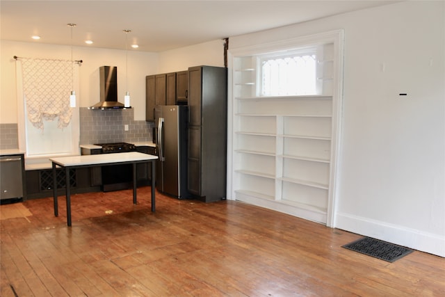 kitchen featuring appliances with stainless steel finishes, backsplash, hardwood / wood-style floors, and wall chimney range hood